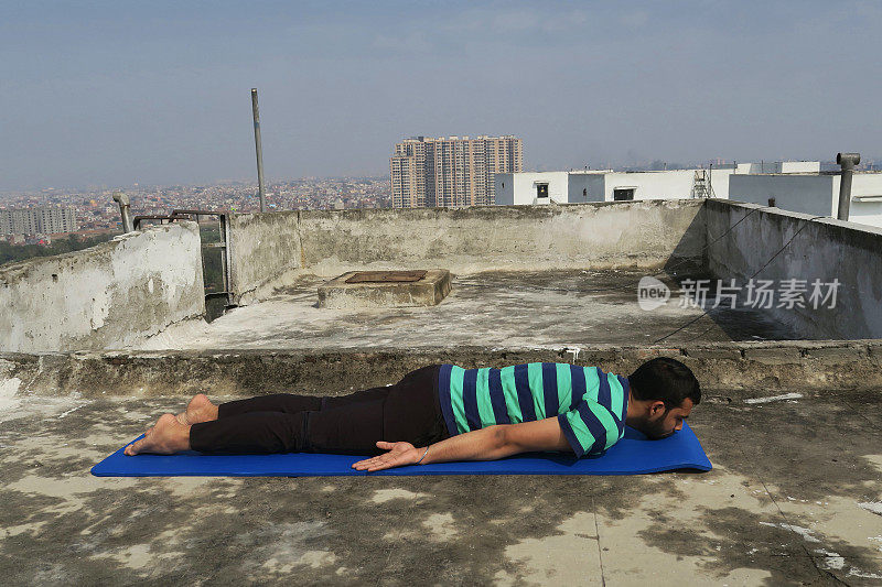 印度人在屋顶上练习前身体(adho mukha savasana)瑜伽姿势，德里，印度